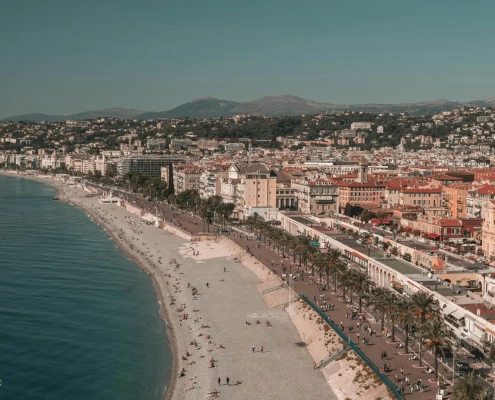Vue panoramique de Nice sur la Côte d’Azur, avec la Promenade des Anglais, la plage de galets, la mer Méditerranée et les collines en arrière-plan.