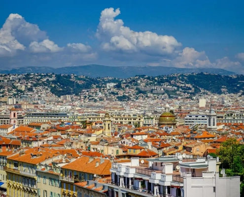 Vue panoramique sur les toits de tuiles orange du Vieux-Nice avec la tour de l'Horloge, le dôme de la cathédrale Sainte-Réparate et les collines de la Côte d'Azur en arrière-plan